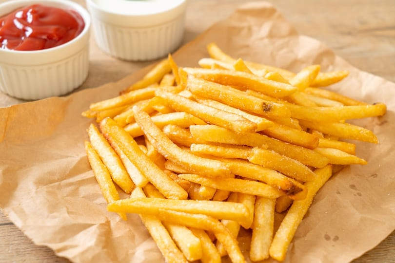 Golden french fries with salt on brown paper, with small white bowls of ketchup and mayonnaise.