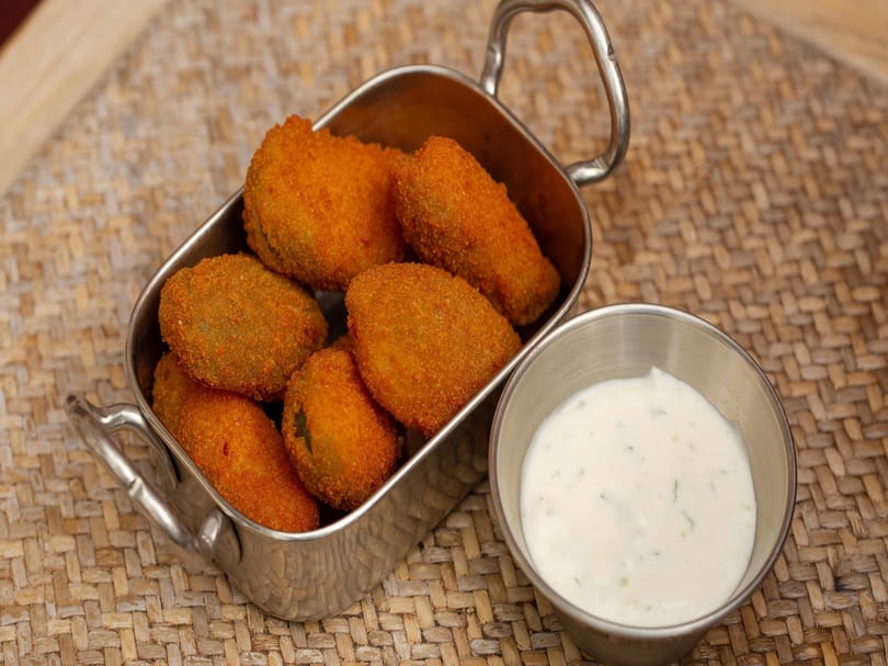 Crispy fried pickles in a metal dish with a side of creamy white dipping sauce.